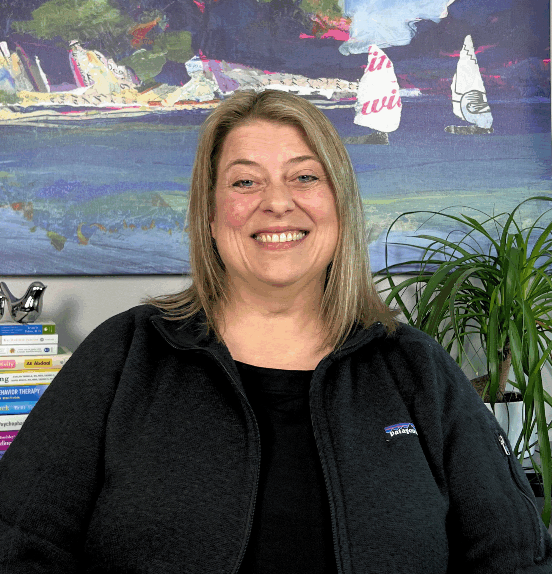 Jill carter, provider at evolve health, smiling in front of a painting of an ocean with sailboats.